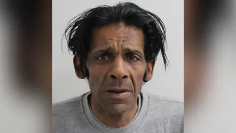 Met Police Man in grey jumper and black hair looks at camera in a police station