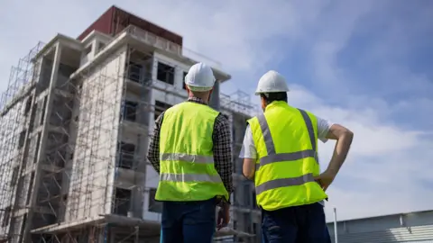 Getty Images Two construction workers looking up at building under construction