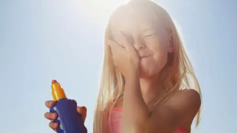 A child applying suncream to their face on a sunny beach 