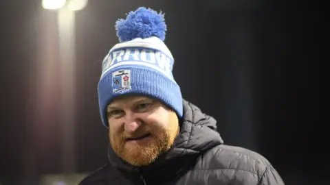 Andy Whing wearing a bobble hat at Barrow's match with Tranmere 