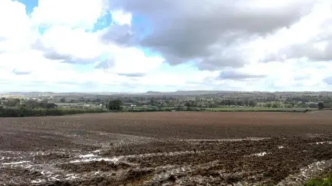 A view over a muddy field with some houses in the distance.