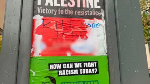 Unknown Graffiti reading ‘Kill More Jews’ written over a pro-Palestine and anti-racism poster on the side of a bus stop shelter.