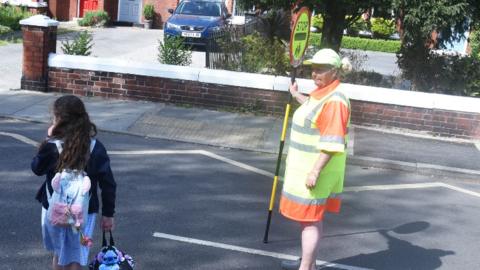 Lollipop lady with child crossing the road
