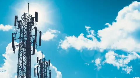 Two telecommunications masts are silhouetted against a bright blue and sunny sky.