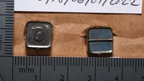 National Crime Agency Two small metal stamps, about a centimetre wide each, next to rulers in an police investigation picture.