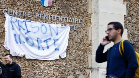A banner reading 'death prison' hangs outside the La Santé penitentiary in Paris