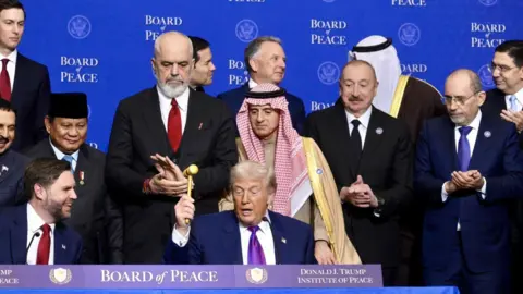 EPA US President Donald Trump raises a gavel during a board of peace meeting in Washington. He is surrounded by other members of the board of peace. 