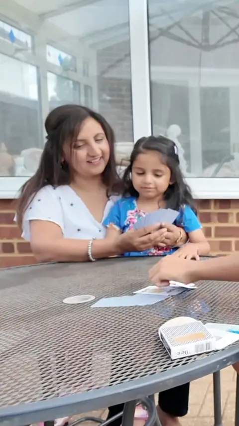 A woman sits with her daughter at a table outside.