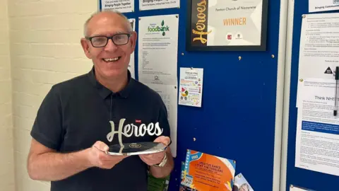 BBC Pastor Trevor Hutton holding an award in a church entrance hall.