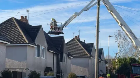 A fire officer on a cherry picker above a fire damaged house