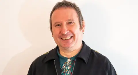 Unison Rad Kerrigan dressed in the Mod style with a "Paul Weller" haircut. He is wearing a paisley pattern shirt and is smiling.