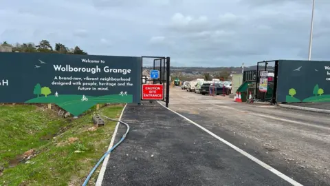 The entrance to the Wolborough site with a sign on the left and cars and vans visible on the site