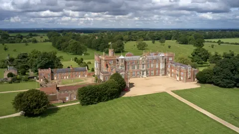 A drone shot of Burton Constable Hall and the grounds surrounding it. The sky is cloudy.