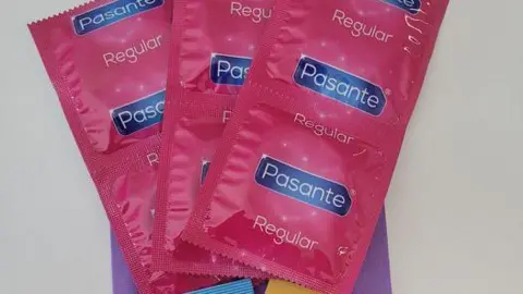 Six condoms and a pack of lube displayed on top of a small, purple paper bag