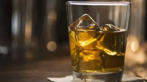 A glass tumbler filled with whisky and ice.