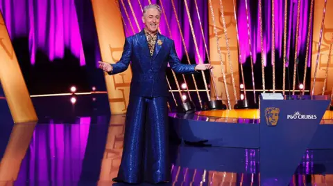 Getty Images Alan Cumming wearing a shiny electric blue suit