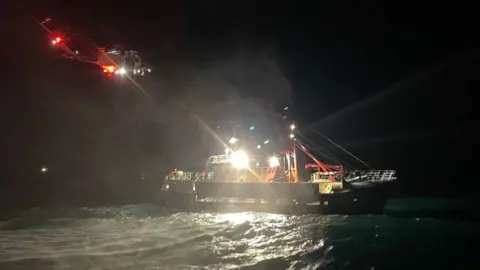 The Honeybourne III fishing boat in darkness, with a Coastguard helicopter overhead.