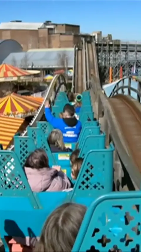 Point of view shot from rollercoaster at summit with people forward facing in blue seats at height