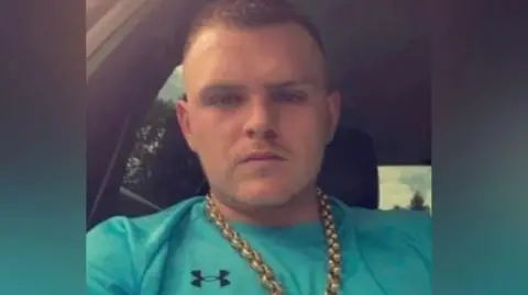 Connor Brookes wearing a green t-shirt and gold chain, taking a selfie