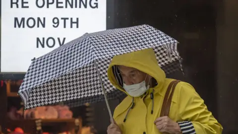 Getty Images A woman wearing a face mask walks past a shop with a sign in the window saying 'opening Mon 9th Nov' on November 1, 2020 in Cardiff, Wales