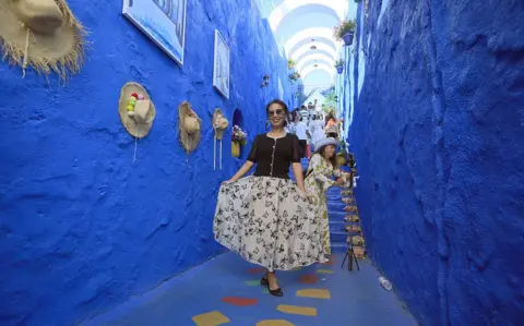 VCG /GETTY IMAGES A woman curtseys for the camera as she and others walk through a bright blue passageway designed to replicate the streets of Chefchaouen.