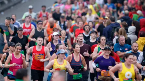 PA Media Runners taking part in the Great North Run. They are wearing colourful running vests, some wear caps and some wear headphones.