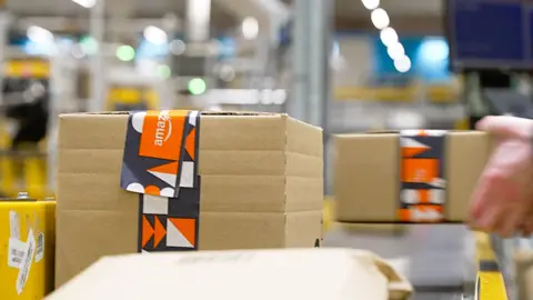 Large cardboard boxes with orange and grey Amazon branded tape roll down a conveyer belt at the company's Swansea warehouse