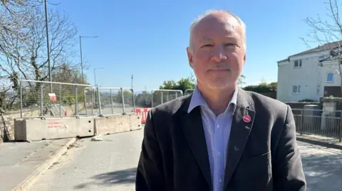 LDRS A man, Jim Dickson, stood in front of a road which has been blocked off by barriers.