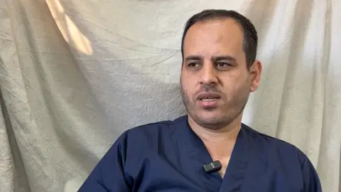 Dr. Ahmed Dhir está em frente a uma tela vestindo uma blusa azul escura