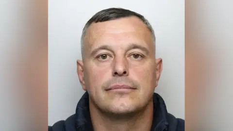 Gareth Whitehouse's mugshot. He is wearing a dark jacket and has short, dark and greying hair.