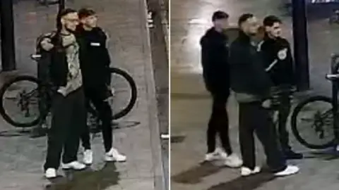 A blurry CCTV image of men standing in the street near a bike rack. They all are wearing dark clothing.