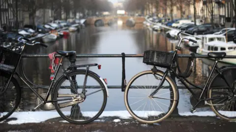 PA Media Two bicycles chained to an iron fence on a bridge. A canal lined with small boats is pictured beyond them.