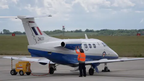 People in orange hi-vis jacket work on a small white aircraft in an airfield