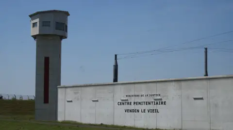 Exterior shot of the Vendin-le-Vieil prison in northern France shows its guard watchtower and high walls and power lines.