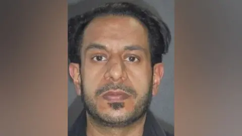 A police mugshot of Yasar Hussain, a man with black hair, a receding hairline, dark eyes and short stubble