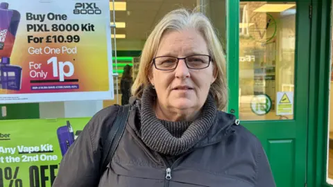 Audrey has short blonde hair. She is wearing glasses.