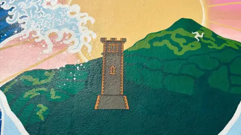 David Britton A close-up of the mural shows a mountain side with the manx symbol, and a castle tower. 