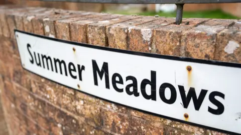 Aodhán Roberts A white and black sign saying 'Summer Meadows' on a red brick wall. 