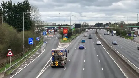 Watford Gap service station photographed from a bridge. There are cars on a lorries on the M1.