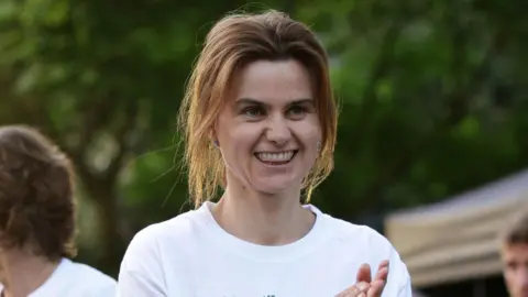 PA Jo Cox wearing a white T-shirt and applauding