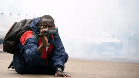 Reuters A Uganda journalists with his camera amid tear gas in Kampala, Uganda - Wednesday 11 July 2018