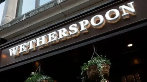 A pub sign which reads "Wetherspoon". There's hanging baskets below.