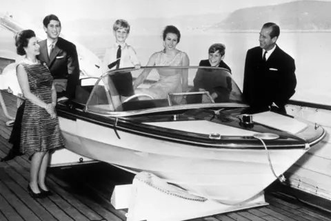 PA Media The royal family's 1969 card features a black-and-white photograph of them gathered around a speed boat on land. All are smartly and formally dressed and smiling. The Queen, the Duke of Edinburgh and Prince Edward are standing. Prince Charles, Princess Anne and Prince Andrew are sitting.
