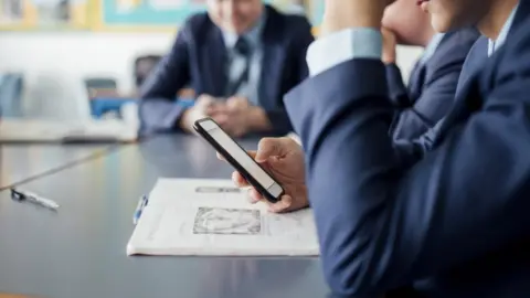 Getty Images A school pupil in uniform using a smartphone at their desk