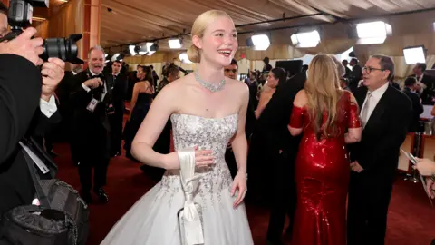 Getty Images Ellie Fanning laughing as she walks past photographers on the red carpet in a white strapless gown 