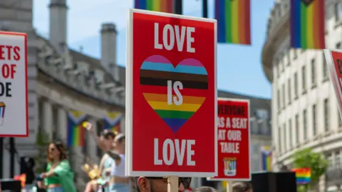 Getty Images A sign at a Pride March in London which reads "love is love" in capital letters with a rainbow heart. A crowd of people can be seen in the back.