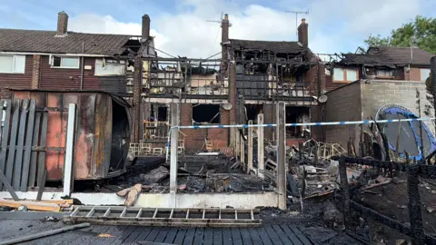 Malik Walton/BBC The back of a burnt out house with blue and white police tape across it
