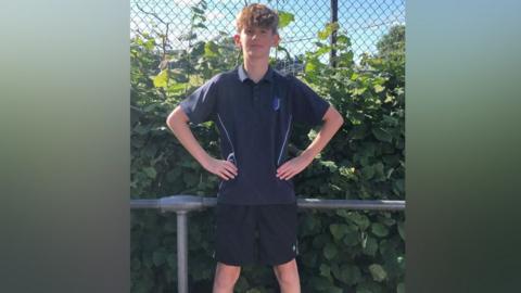A boy wearing a school PE kit of shirt and shorts