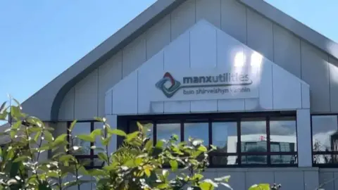 The Manx Utilities company logo on the front of its headquarters building in Douglas. The building is grey with a peak roof.