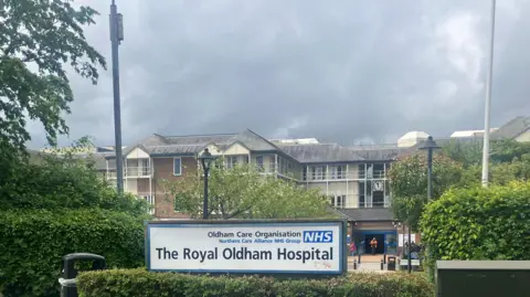 Richard Stead/BBC Exterior of Royal Oldham Hospital with a sign in the foreground and the hospital in the background